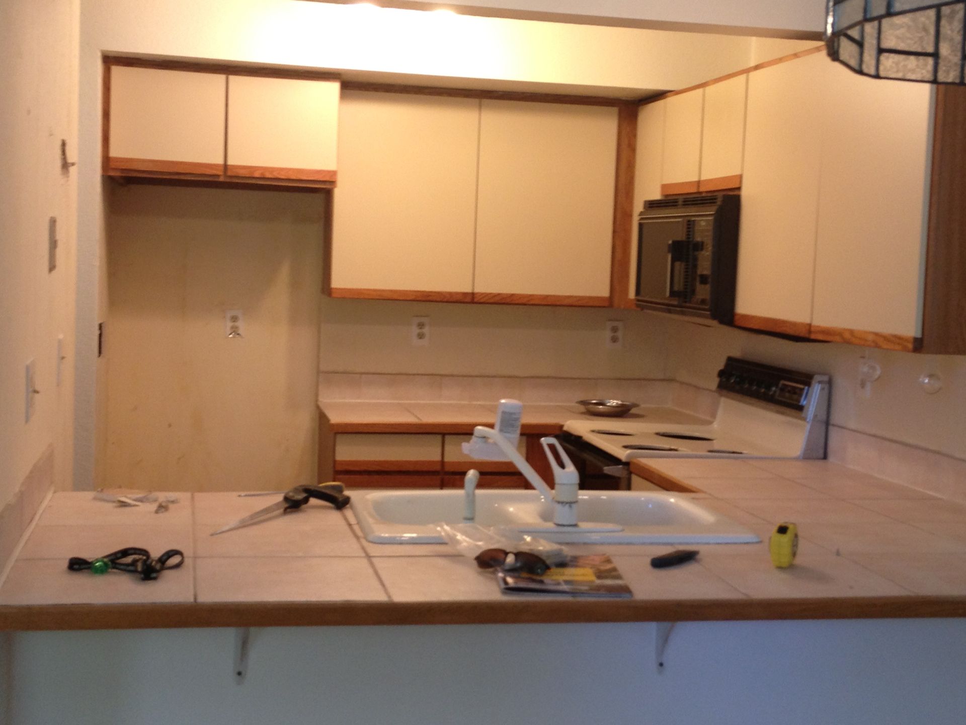 Kitchen with cream cabinets and countertop cluttered with tools and items around a sink.