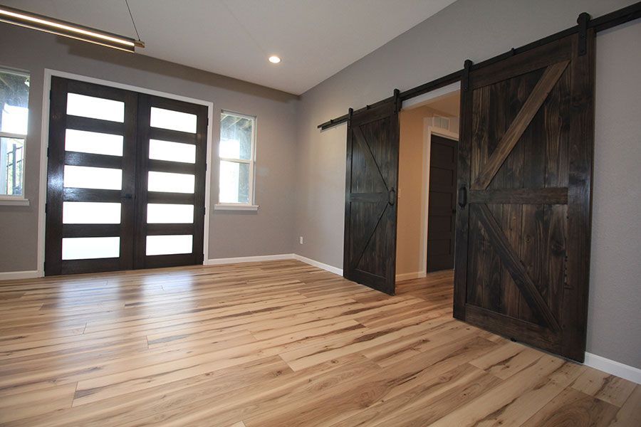 Empty modern room with light wood floors, gray walls, and dark barn doors.