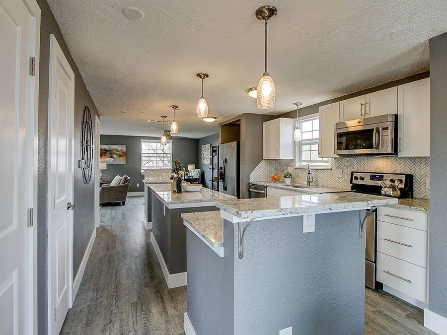 Bright modern kitchen with gray island, white cabinets, pendant lights, and open view to living area.