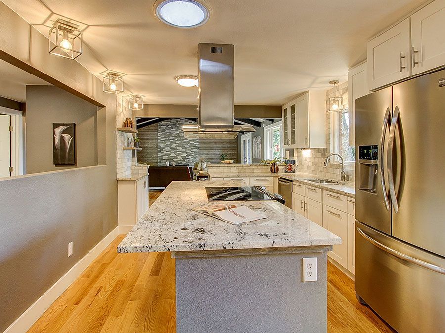 Modern kitchen with white cabinets, granite island, stainless steel fridge, and wood floor.