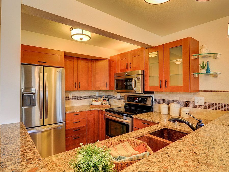 Modern kitchen with stainless steel appliances, wood cabinets, granite counters, and a tiled backsplash