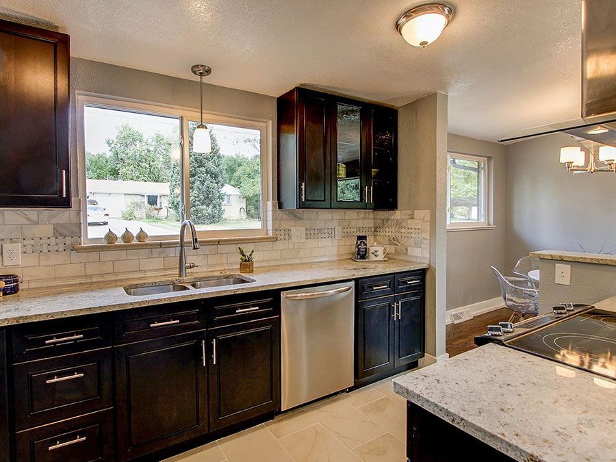 Modern kitchen with dark wood cabinets, granite counters, stainless dishwasher, and a large window over the sink