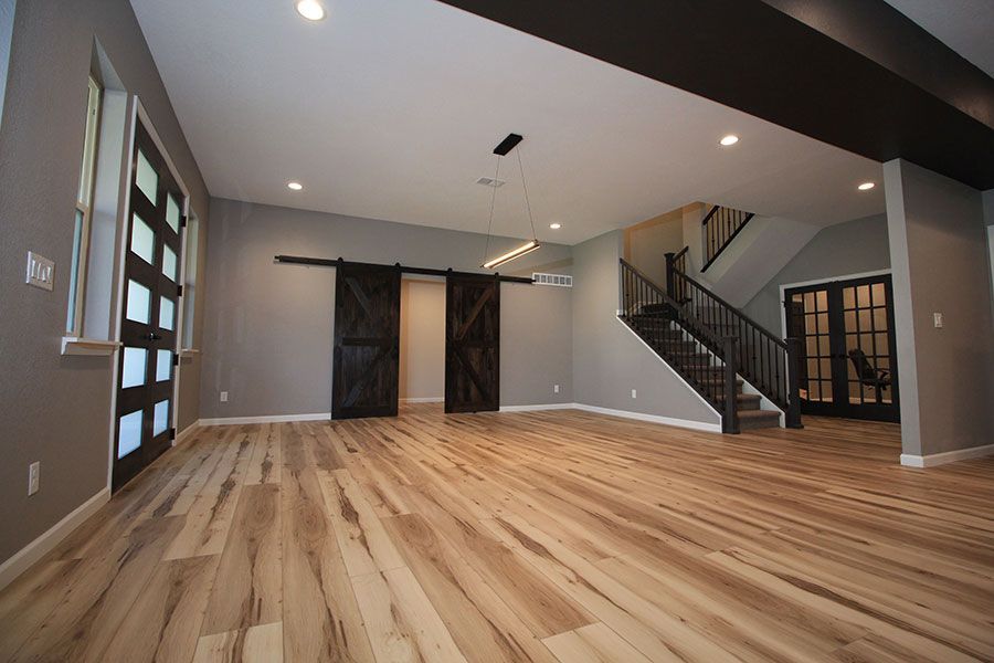 Empty modern living room with hardwood floors, gray walls, stairway, and a black sliding barn door.