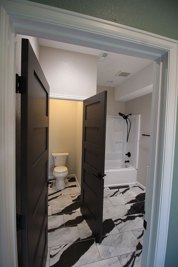 Bathroom with open dark doors, black-and-white floor, toilet, and shower visible inside.