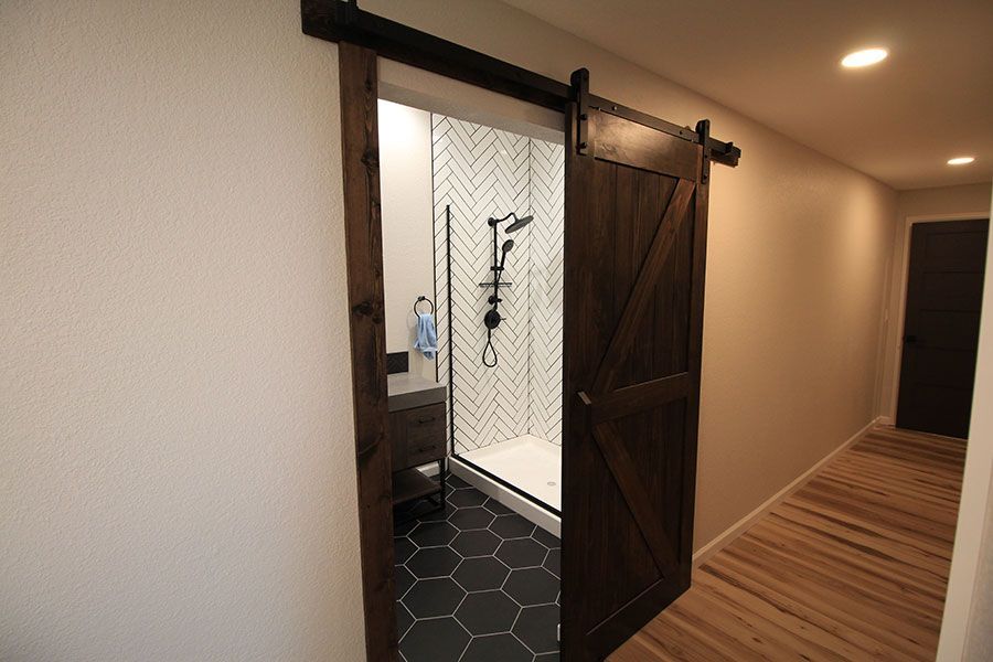 Sliding wooden barn door opens to a bathroom with black hex tile and a shower.