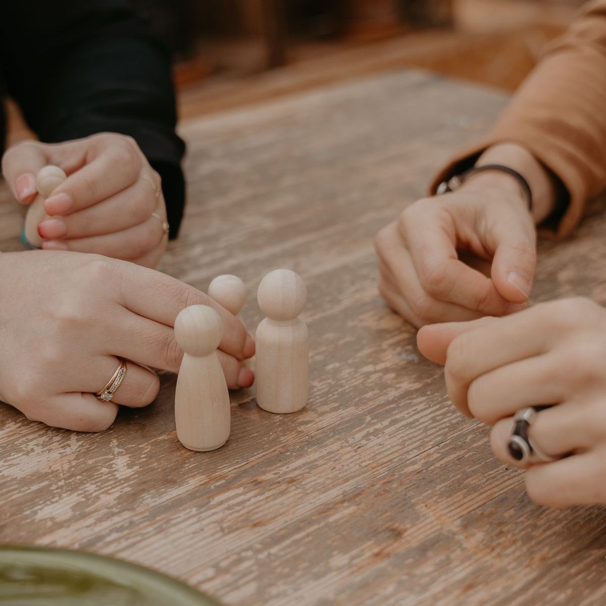 Twee paar handen die met kleine houten figuurtjes spelen op een rustieke houten tafel.