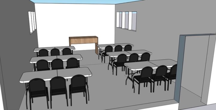 Sala de aula vazia com fileiras de carteiras voltadas para um pódio e um quadro branco.