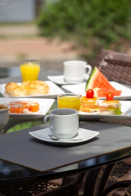 Mesa de café ao ar livre com café, suco e uma variedade de doces para o café da manhã em pratos brancos.