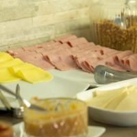 Mesa de bufê com queijo fatiado, frios e pequenas tigelas de condimentos.