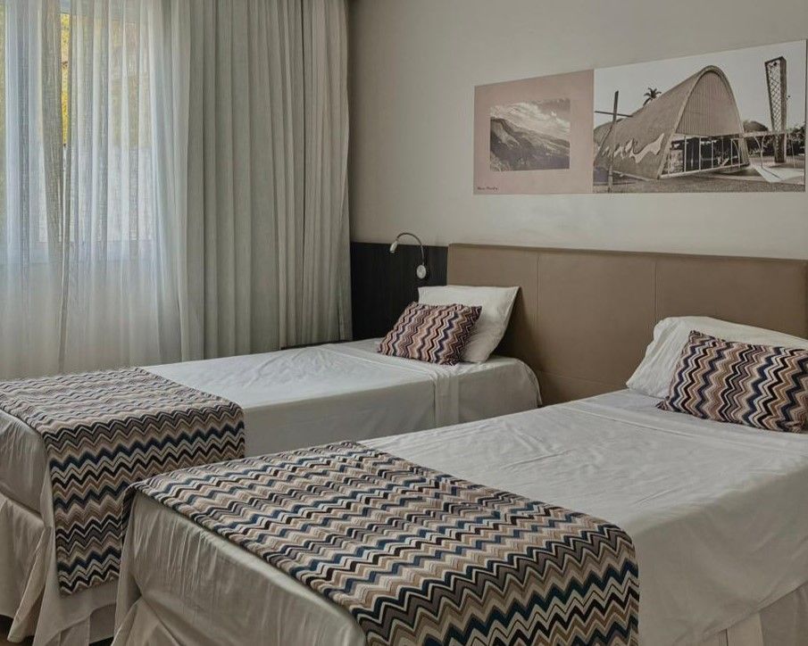 Duas camas de solteiro bem arrumadas em um quarto de hotel bege com mesinhas de cama estampadas e obras de arte na parede.