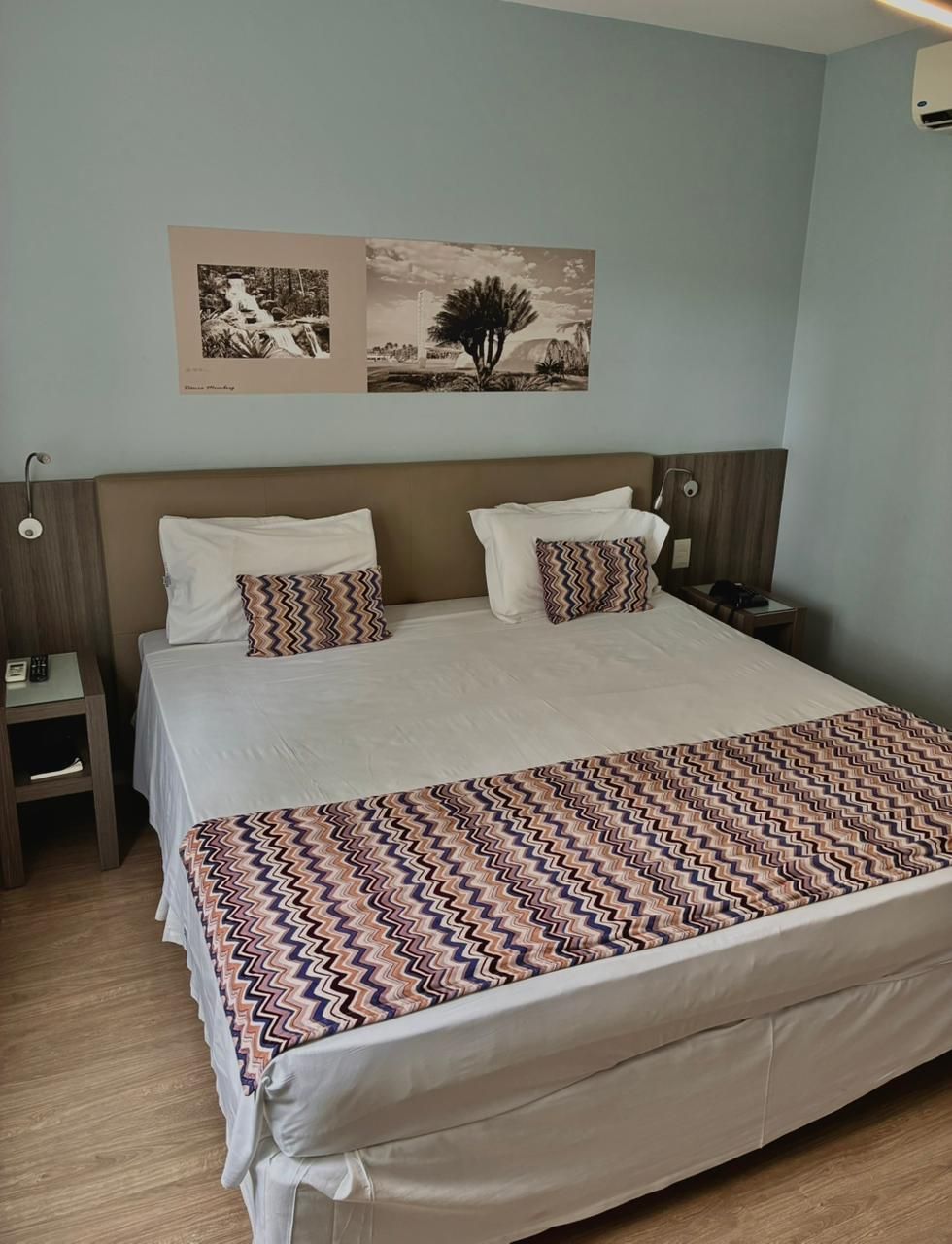 Cama arrumada com peseira e almofadas estampadas em um quarto azul claro.