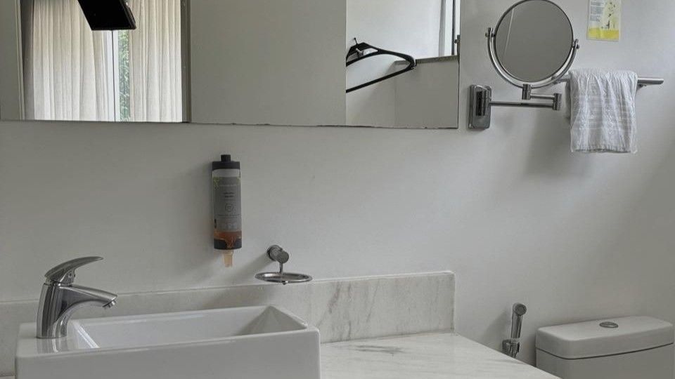 Banheiro moderno com pia branca, espelho, porta-toalhas de parede e vaso sanitário à direita.