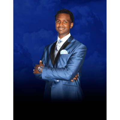 Man in a blue suit standing with arms crossed against a blue studio backdrop.