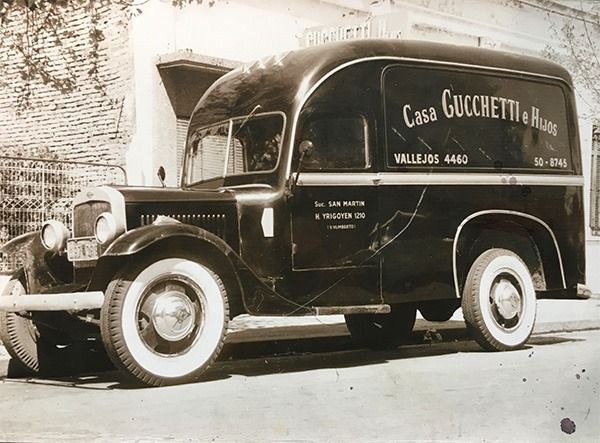 Camioneta de reparto negra de época, estacionada junto a un muro, con la inscripción 