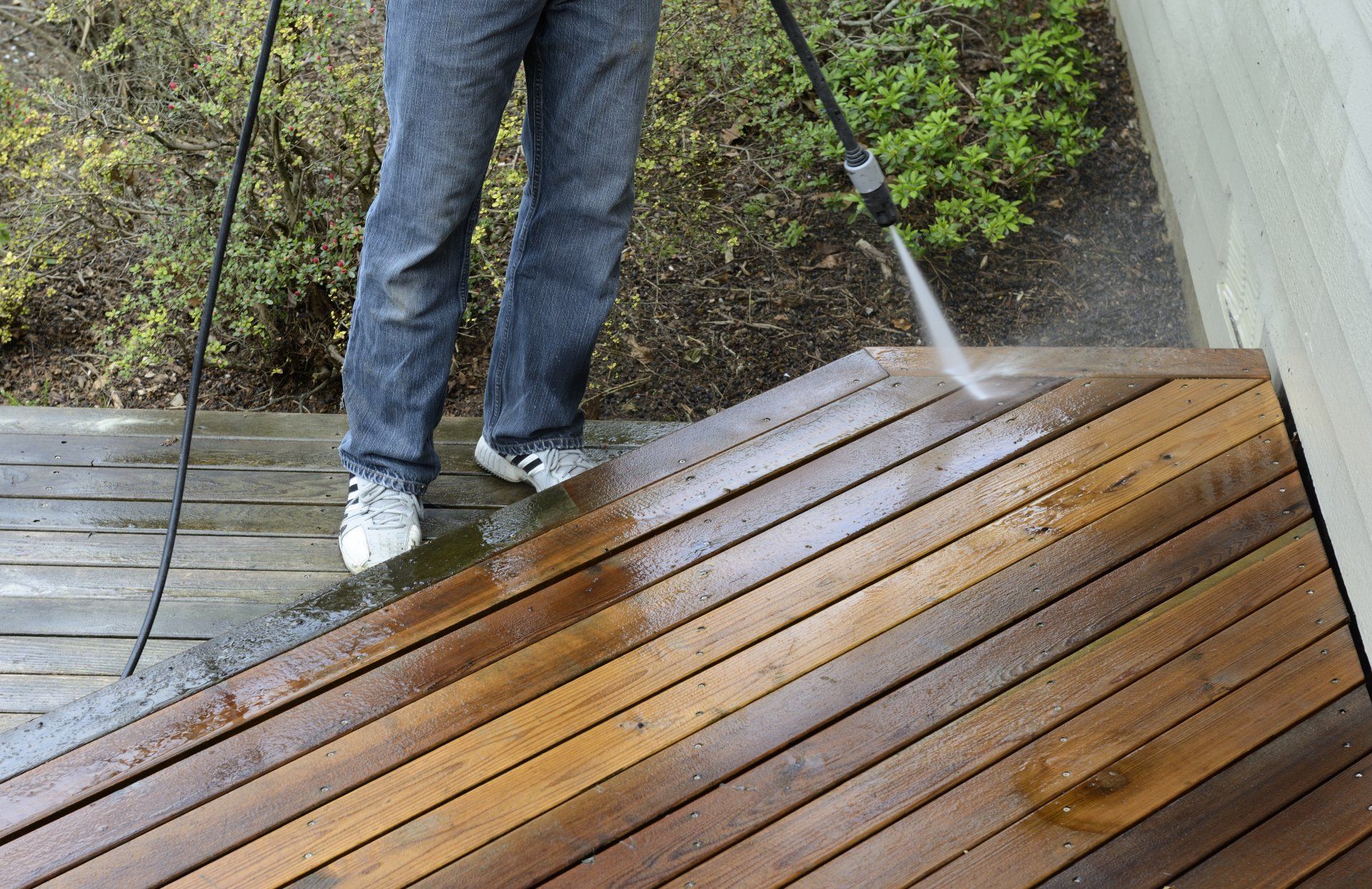 A man is cleaning a wooden deck with a high pressure washer.