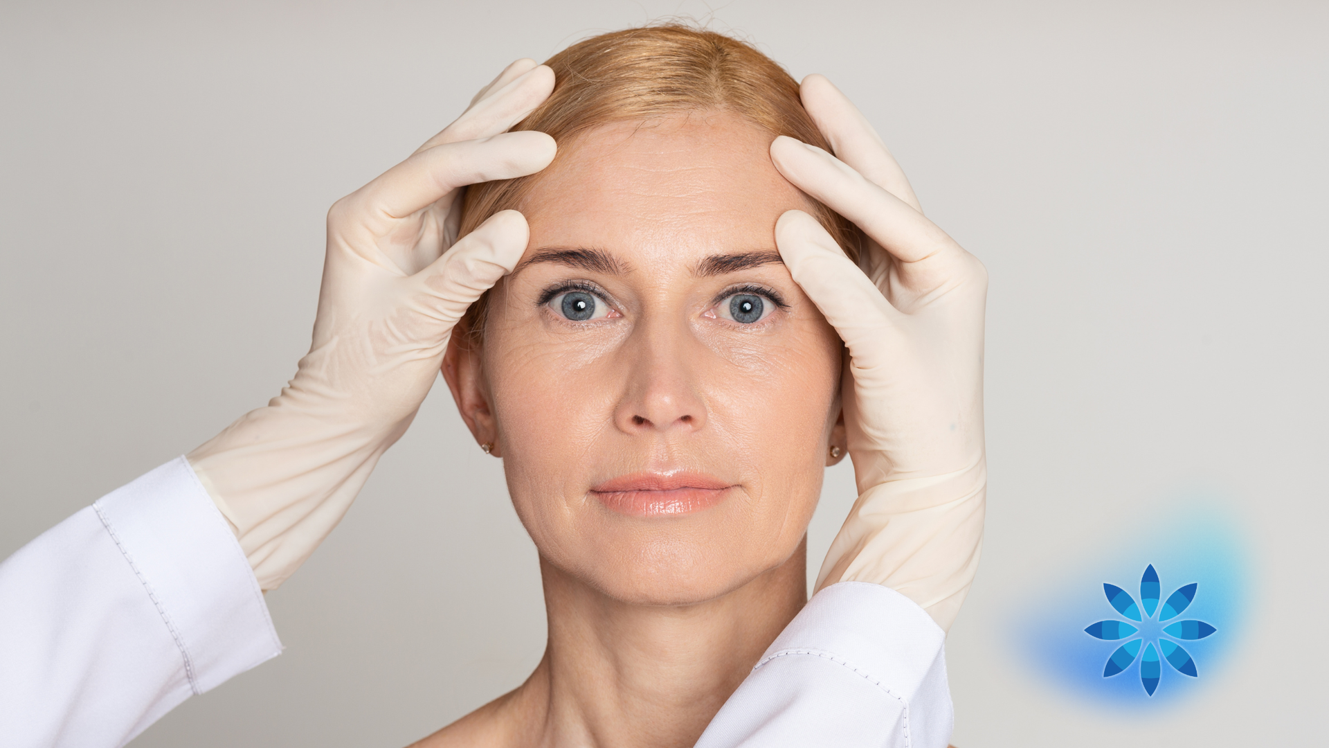 Doctor wearing white gloves examining a woman’s forehead and temples against a plain background