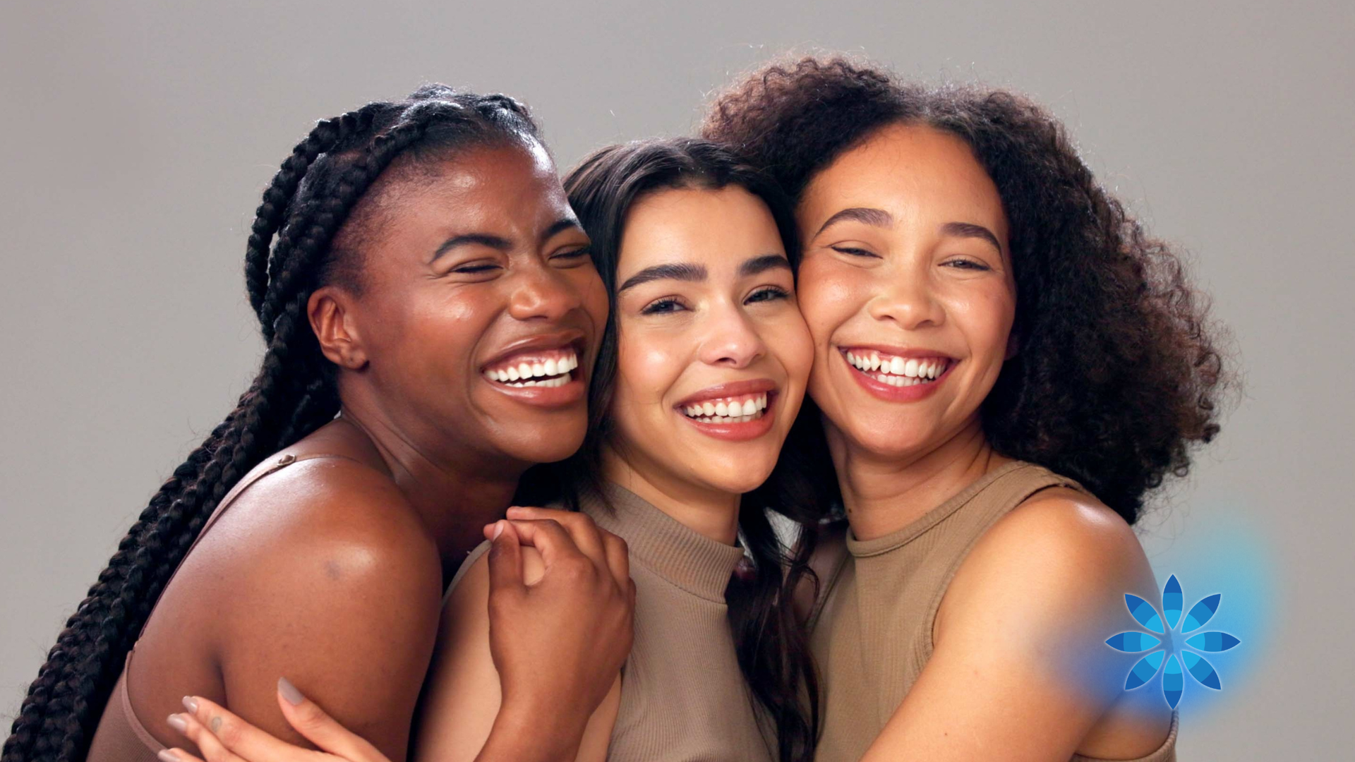 Three smiling friends hugging together against a gray background