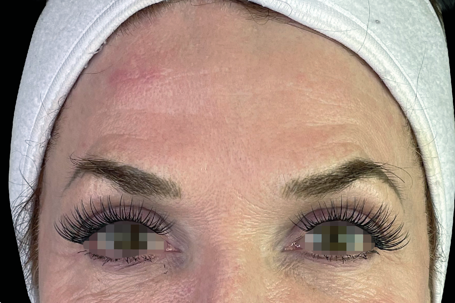 Close-up of a person wearing a white head covering and dramatic false eyelashes, eyes centered in frame