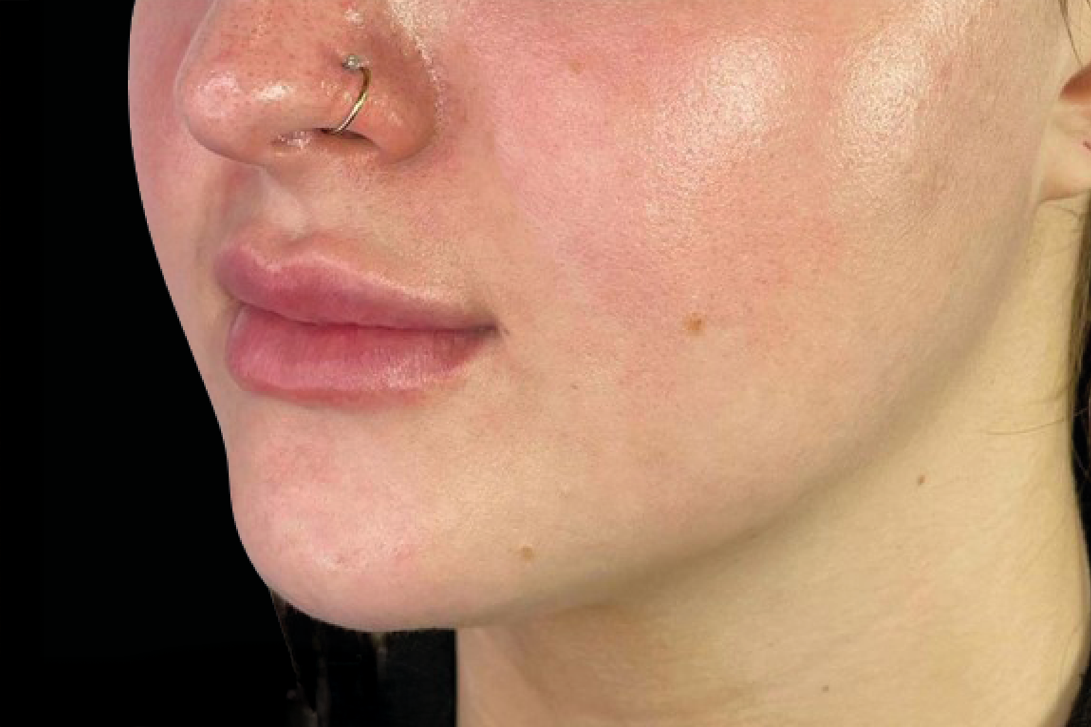 Close-up of a person’s face with a nose ring and natural makeup against a black background