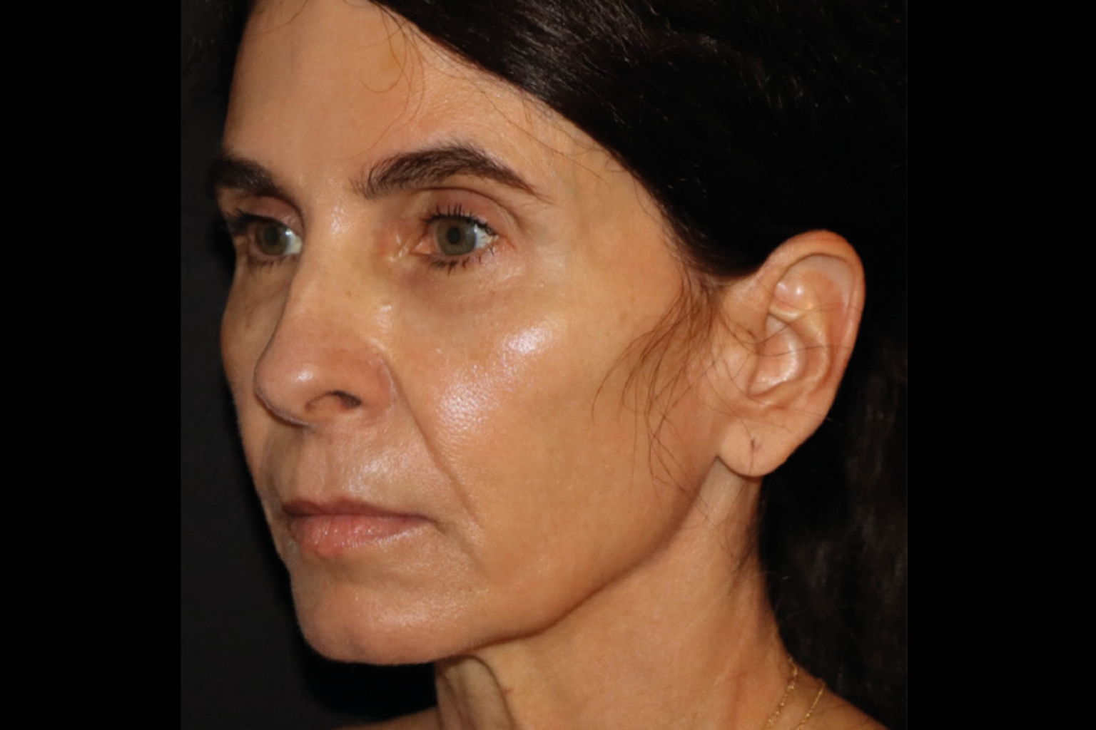Close-up profile of a woman with dark hair against a black background, looking ahead with a neutral expression