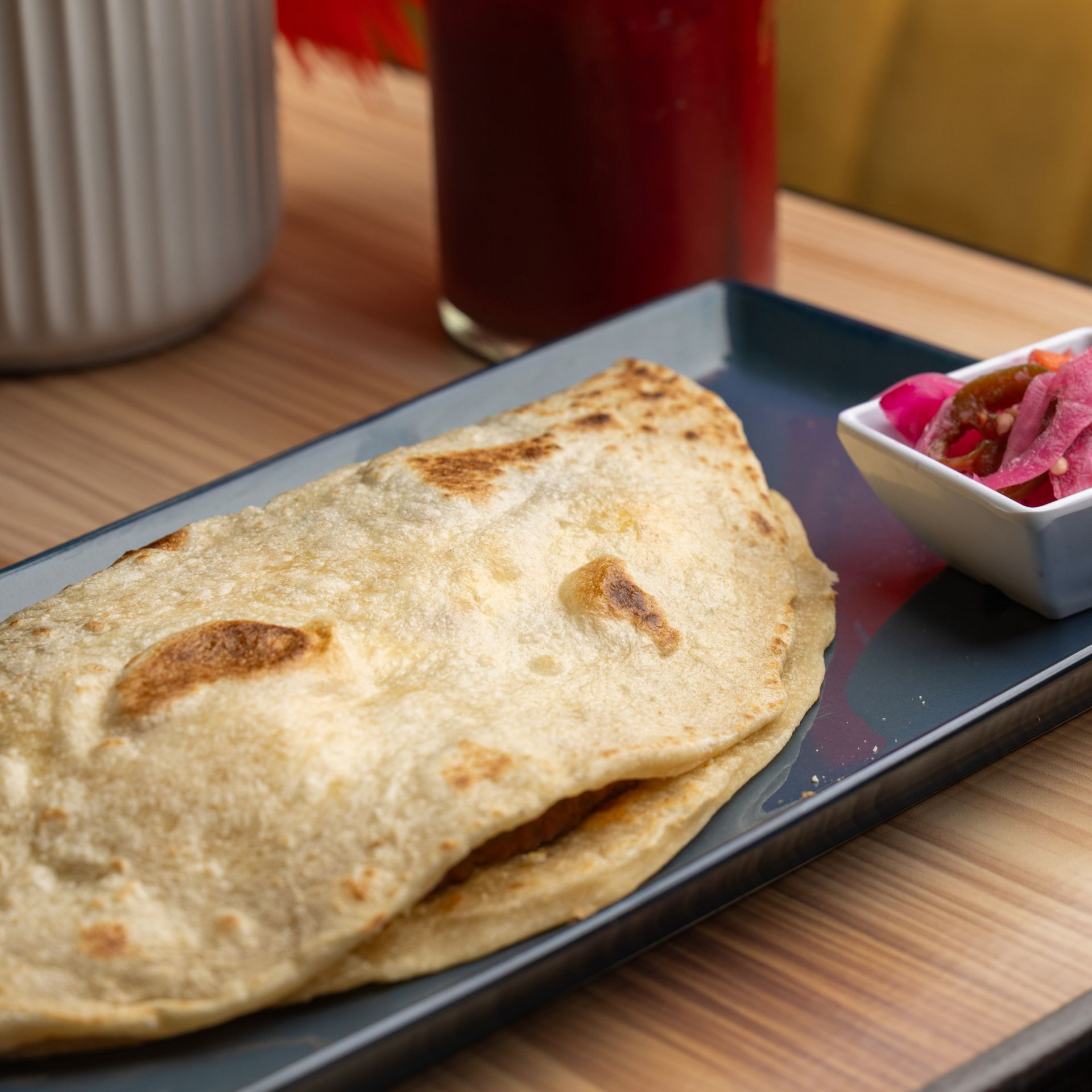 Quesadilla on blue plate with small white bowl of pickled onions, drink in background.