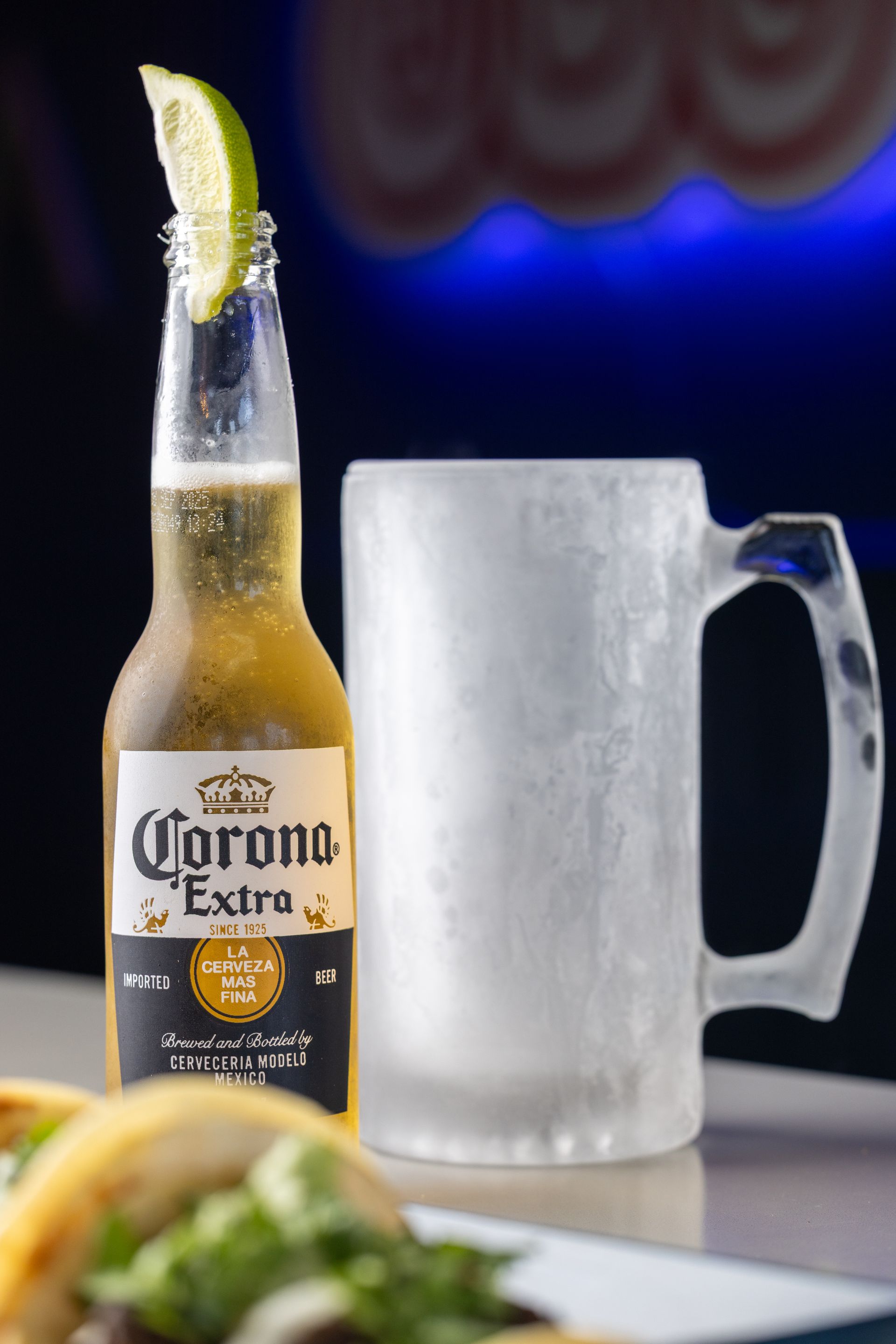 Corona beer bottle with lime wedge, frosted mug, tacos.
