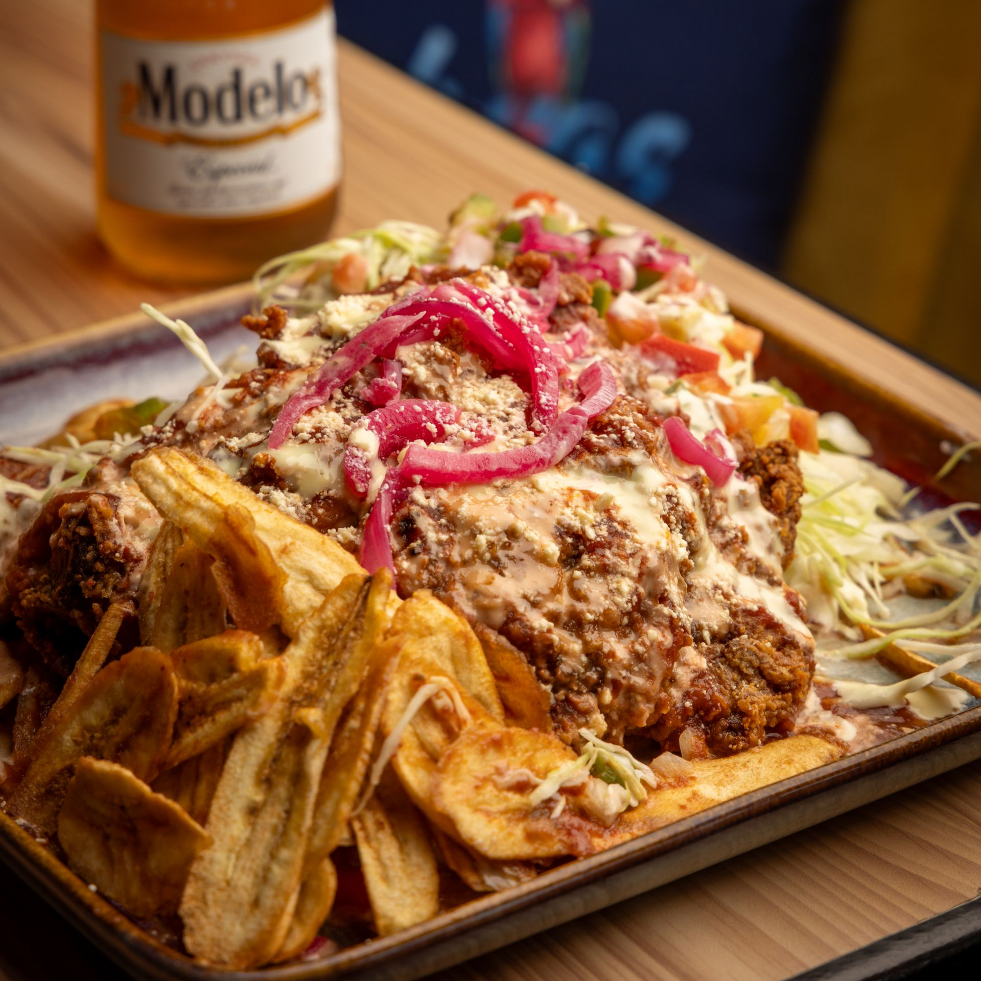 Fried chicken platter with plantain chips, pickled onions, salsa, and a beer bottle.