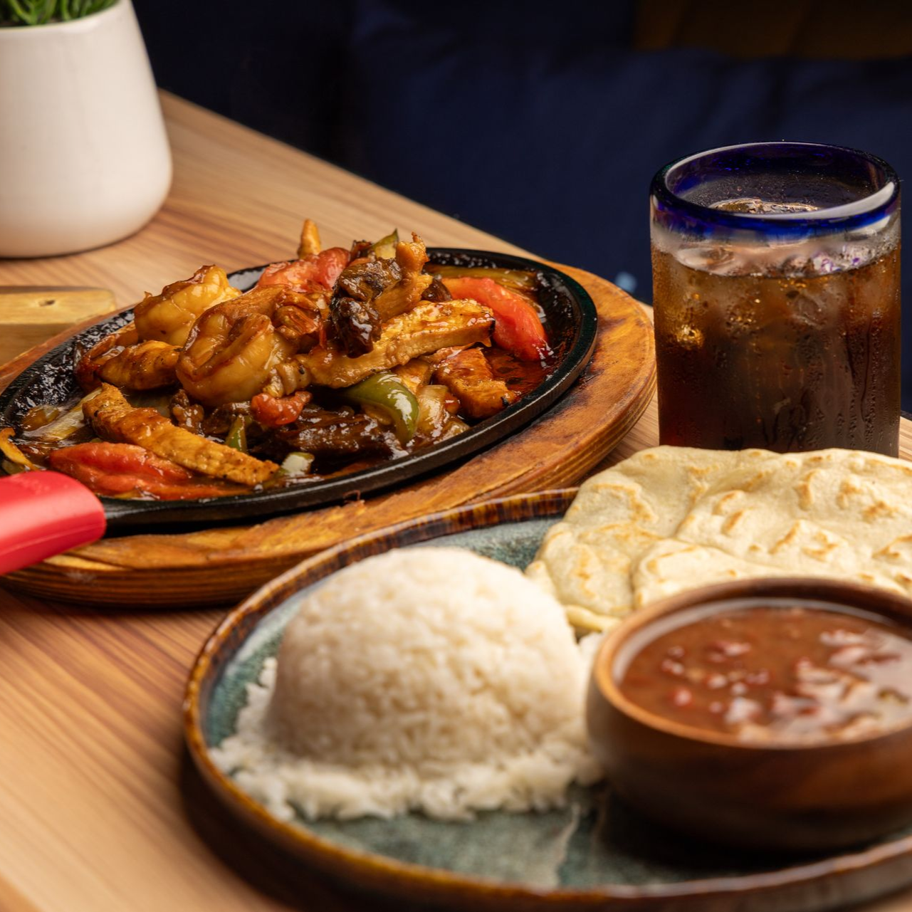 Sizzling fajitas with rice, tortillas, and drink on a wooden table.