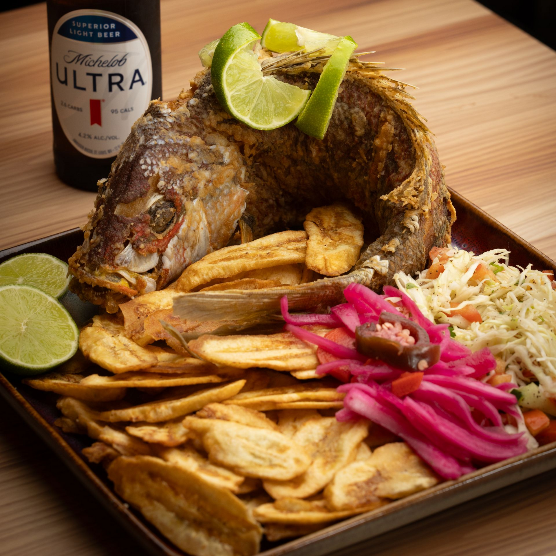 Fried fish with plantain chips, lime, pickled onions, coleslaw, and beer.