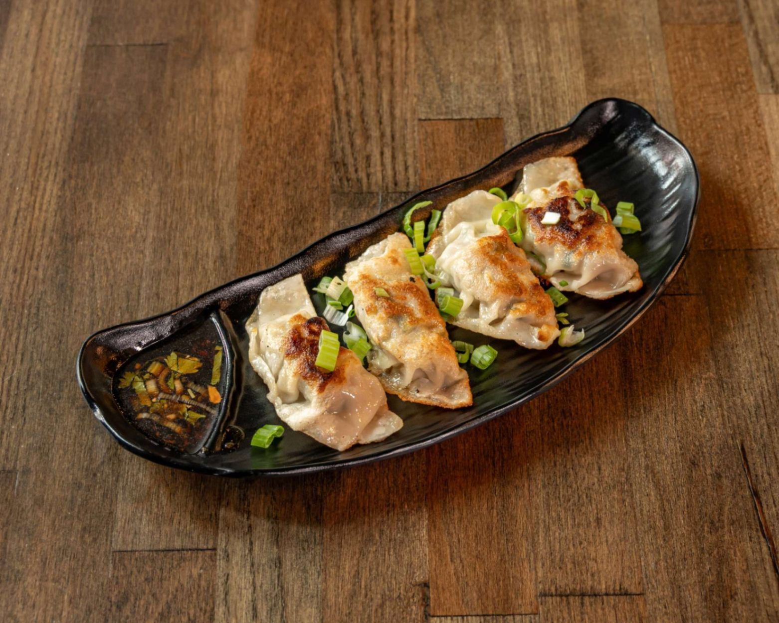 Sushi dumplings topped with sauce and scallions on a black plate on a wooden table