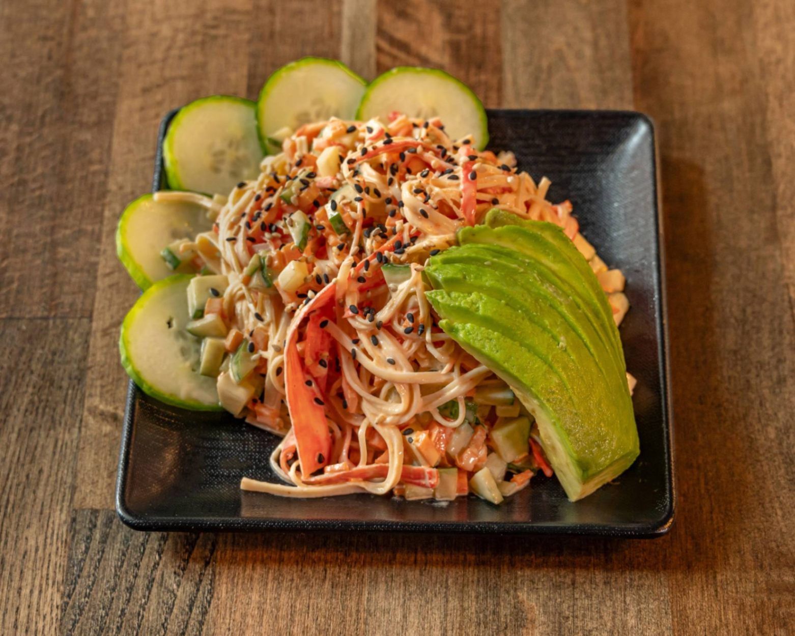 Colorful noodle salad with avocado slices and sesame seeds on a black plate