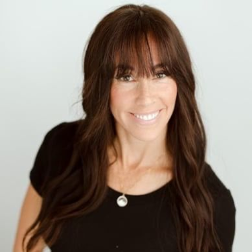 A woman wearing glasses and a gray shirt is smiling for the camera.