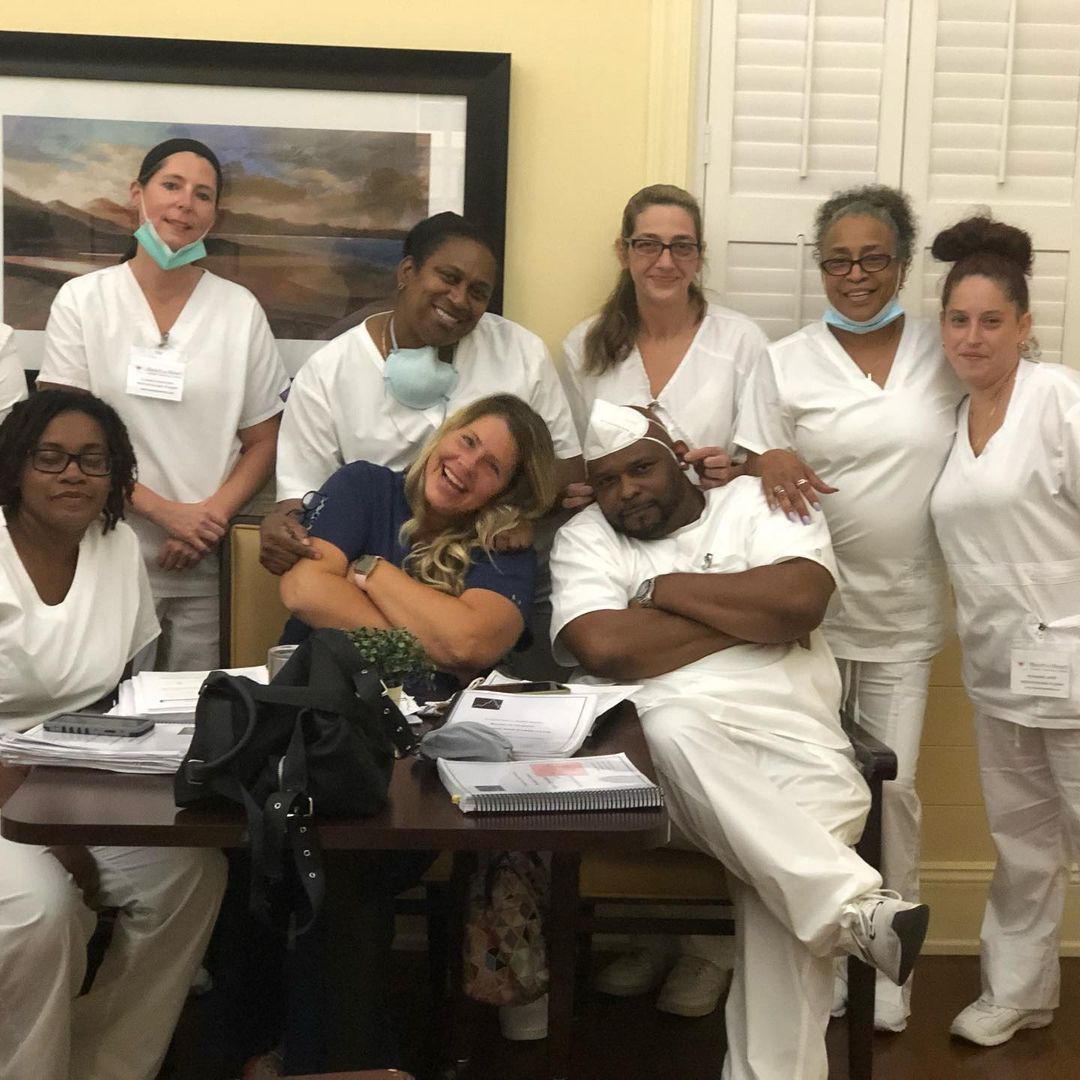 Group of people in white scrubs, smiling around a table with papers.