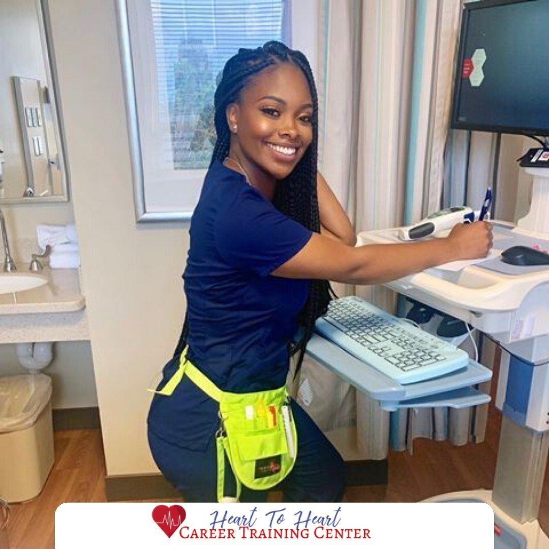 Smiling person in scrubs at a computer in a hospital room.