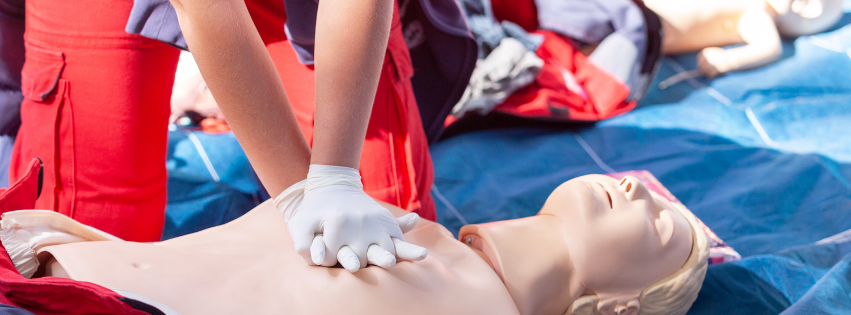 Person in red uniform performing CPR on a training dummy. White gloves on hands compressing chest.