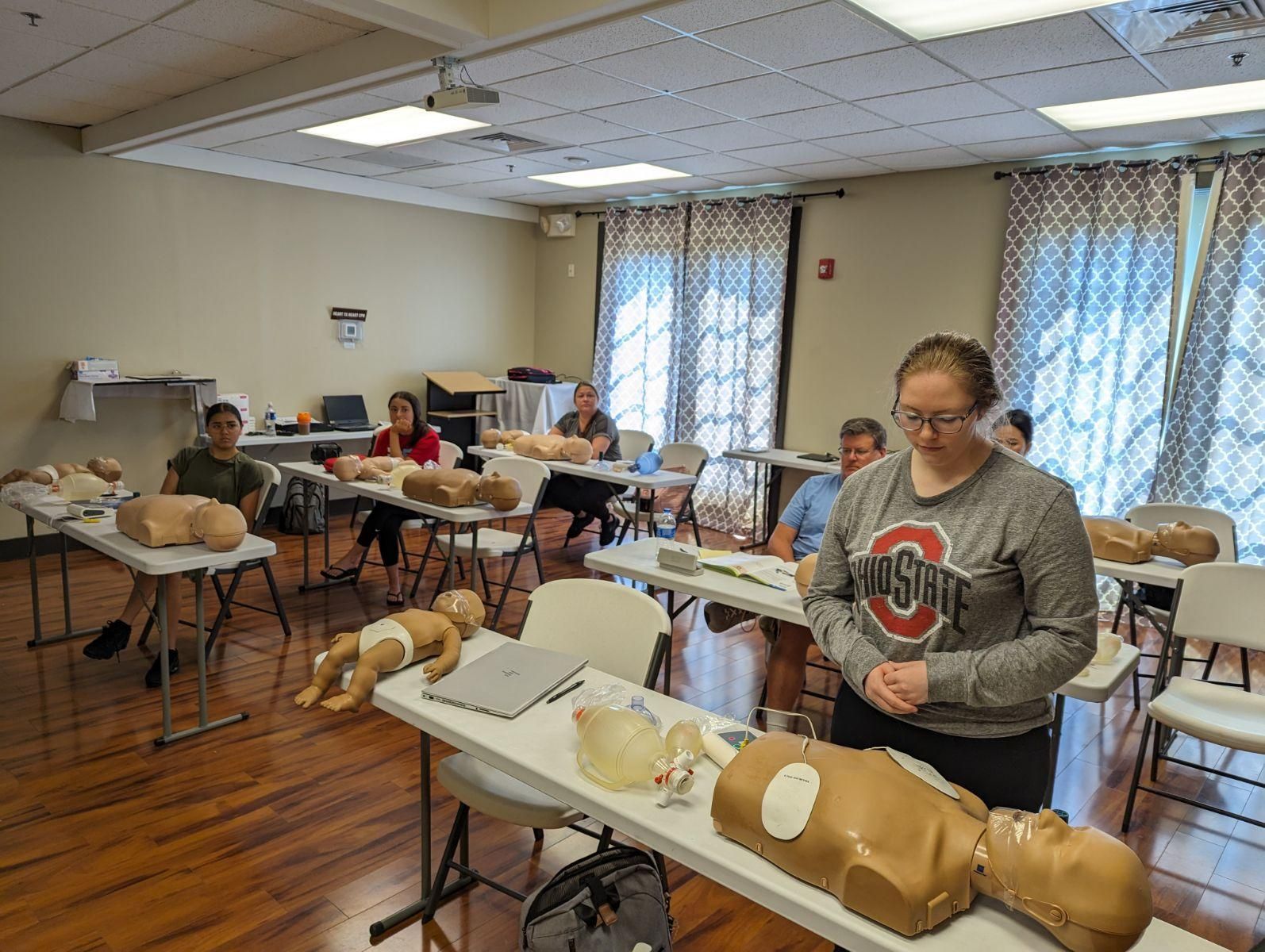 People in a classroom learning first aid; mannequins on tables.