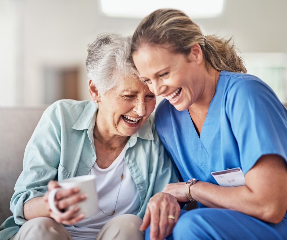 Nurse and elderly woman laughing together indoors; woman holds a mug.