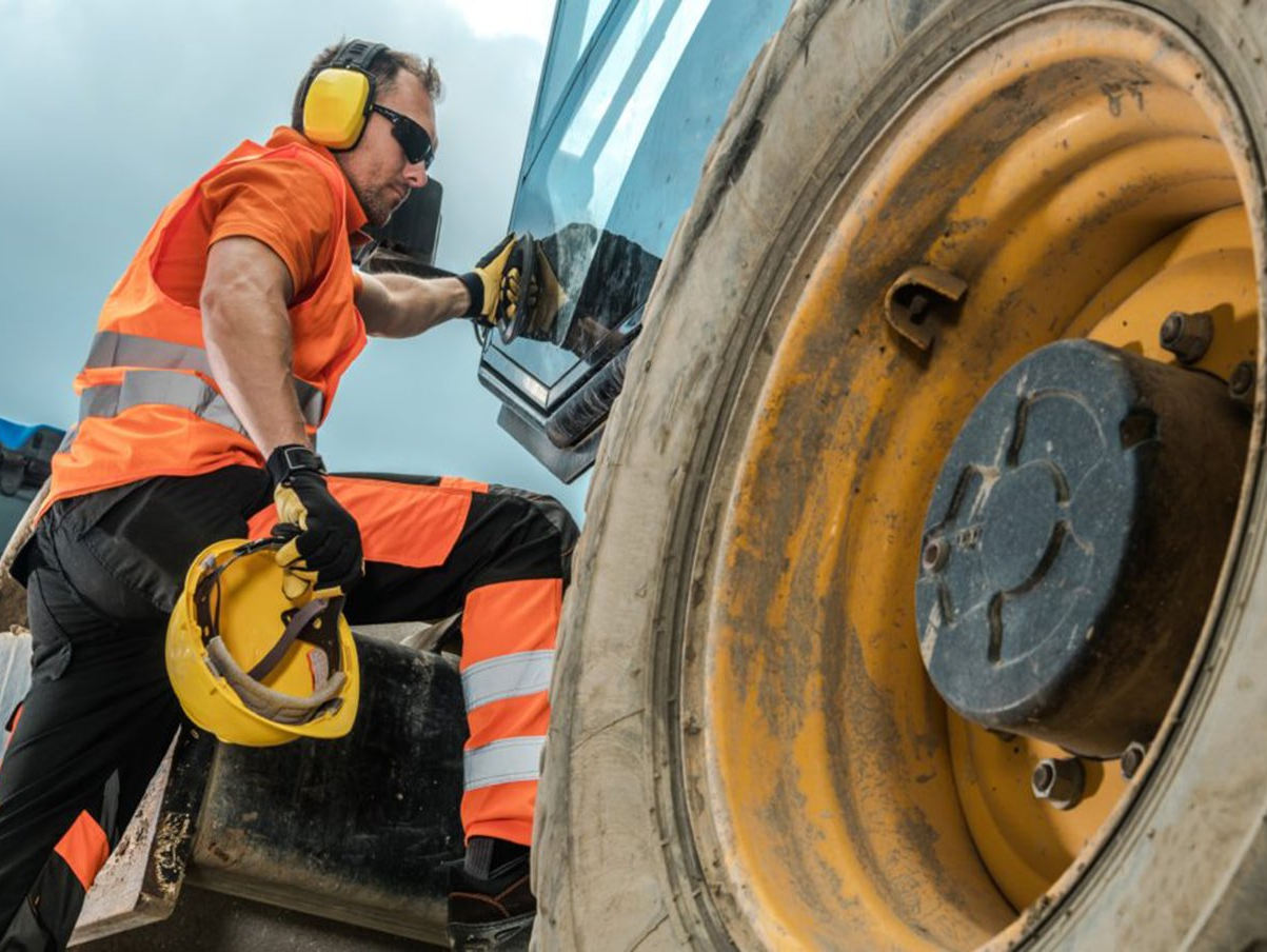 A man wearing headphones and a hard hat is working on a tractor.