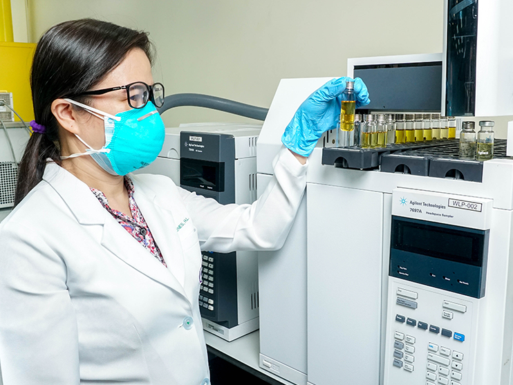 A woman wearing a mask and gloves is working in a lab.