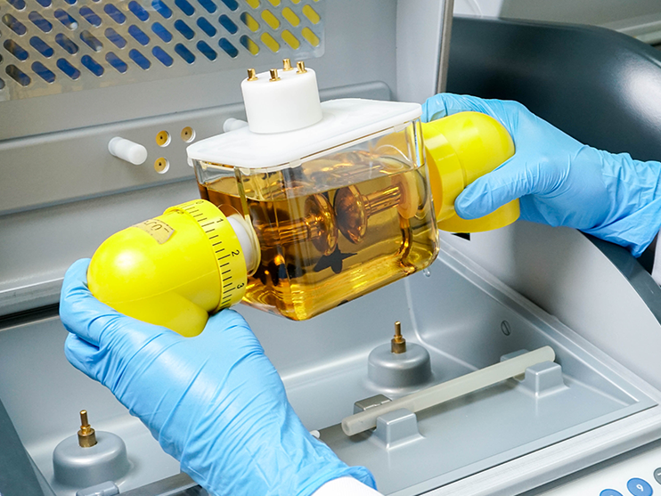 A person wearing blue gloves is holding a yellow container of liquid