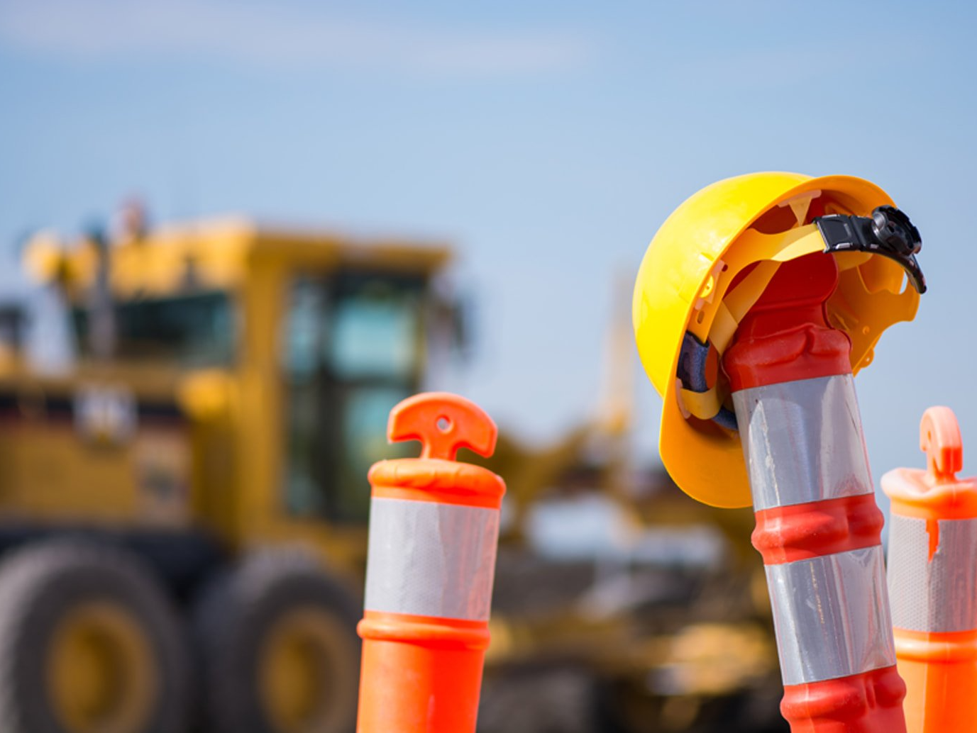 A yellow hard hat is sitting on top of an orange cone at a construction site.