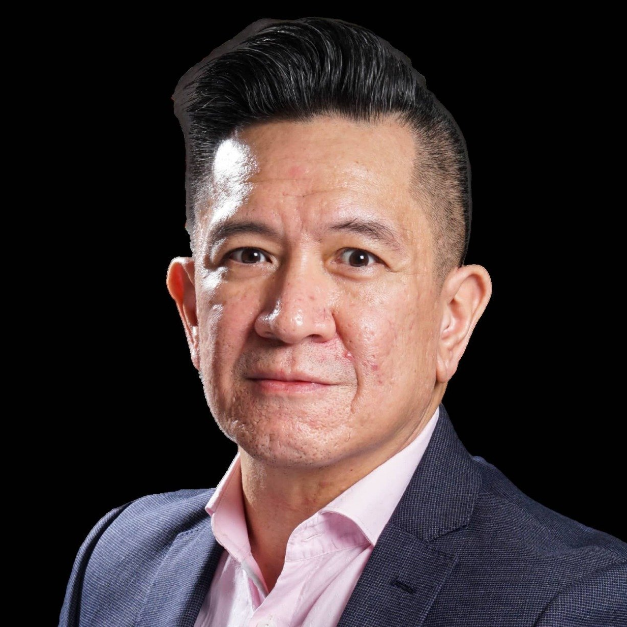 A man in a suit and pink shirt is standing in front of a black background.