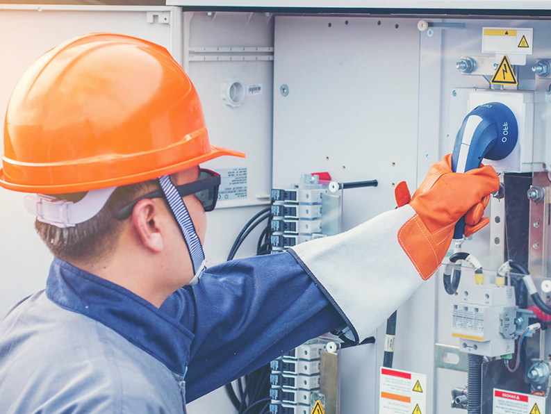 A man wearing a hard hat and gloves is working on an electrical box.
