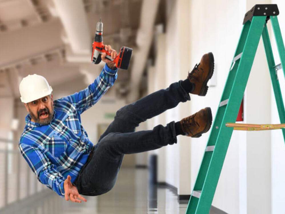 A man is falling off a ladder while holding a drill.