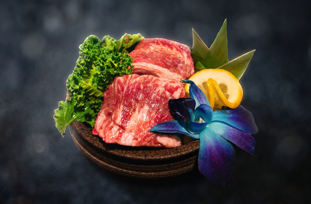 Plated marbled steaks with parsley, lemon wedge, and purple flower on a dark background
