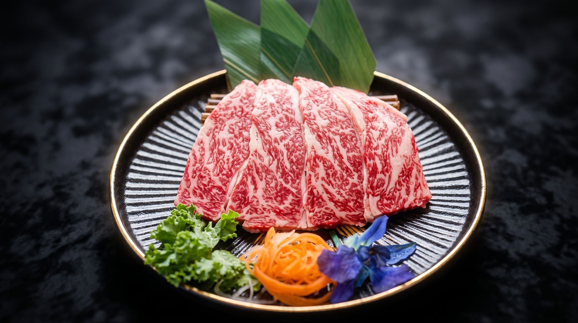 Marbled raw beef arranged on a black plate with green leaves and orange garnish