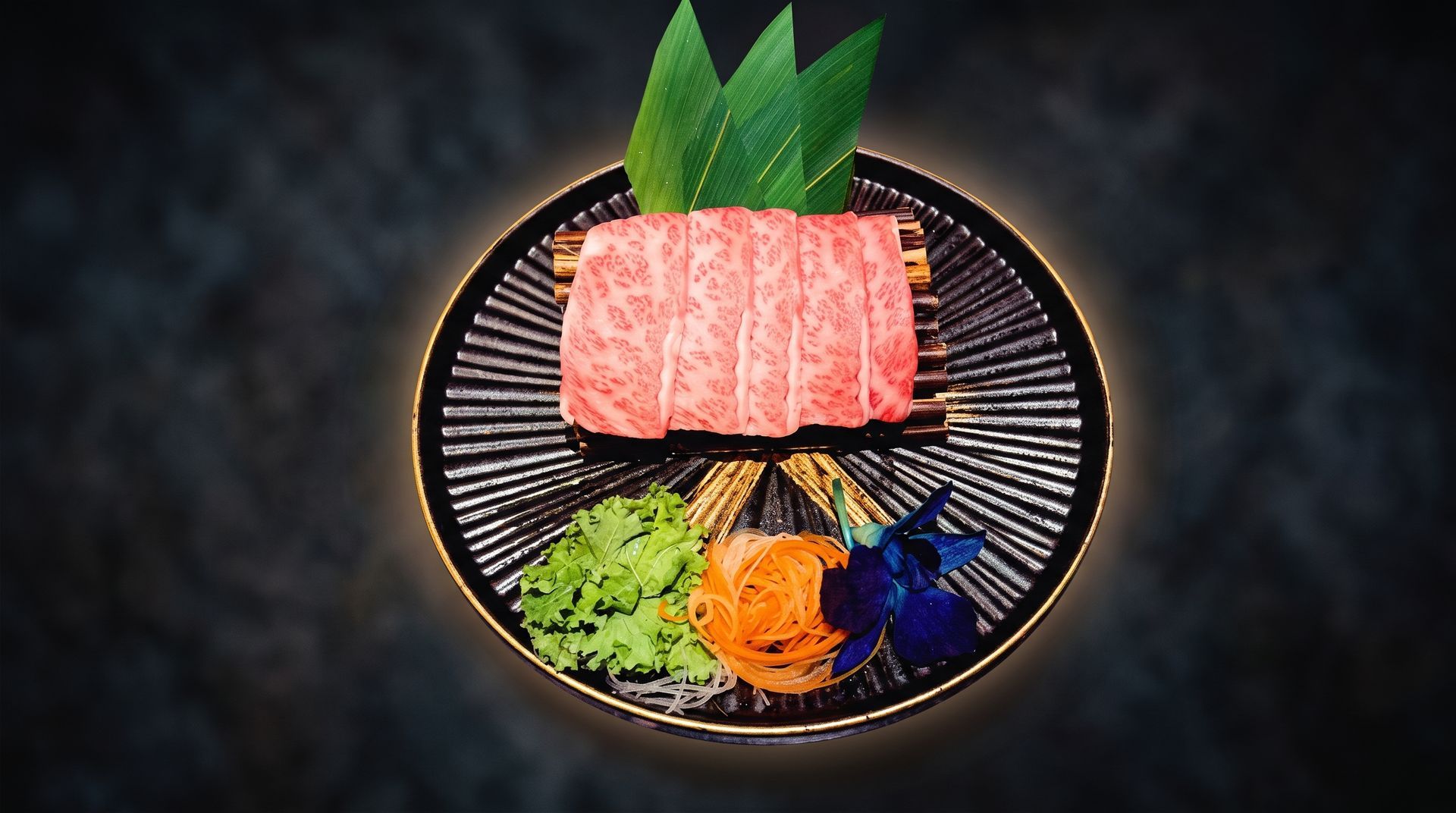 Raw marbled meat slices on a black plate with green leaves and colorful garnish on a dark background