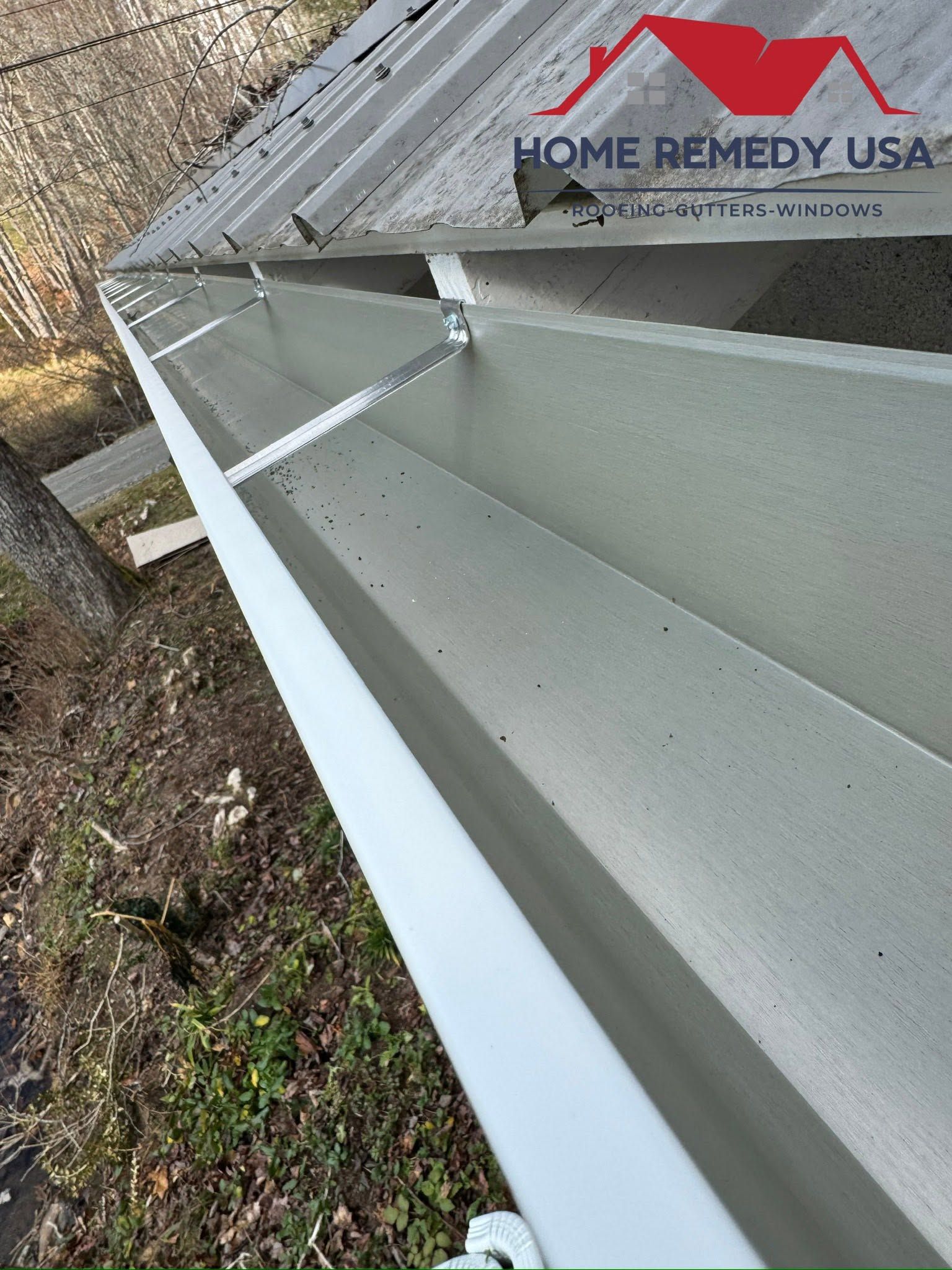 Rain gutter and roof edge beside a Home Remedy USA sign on a building exterior.