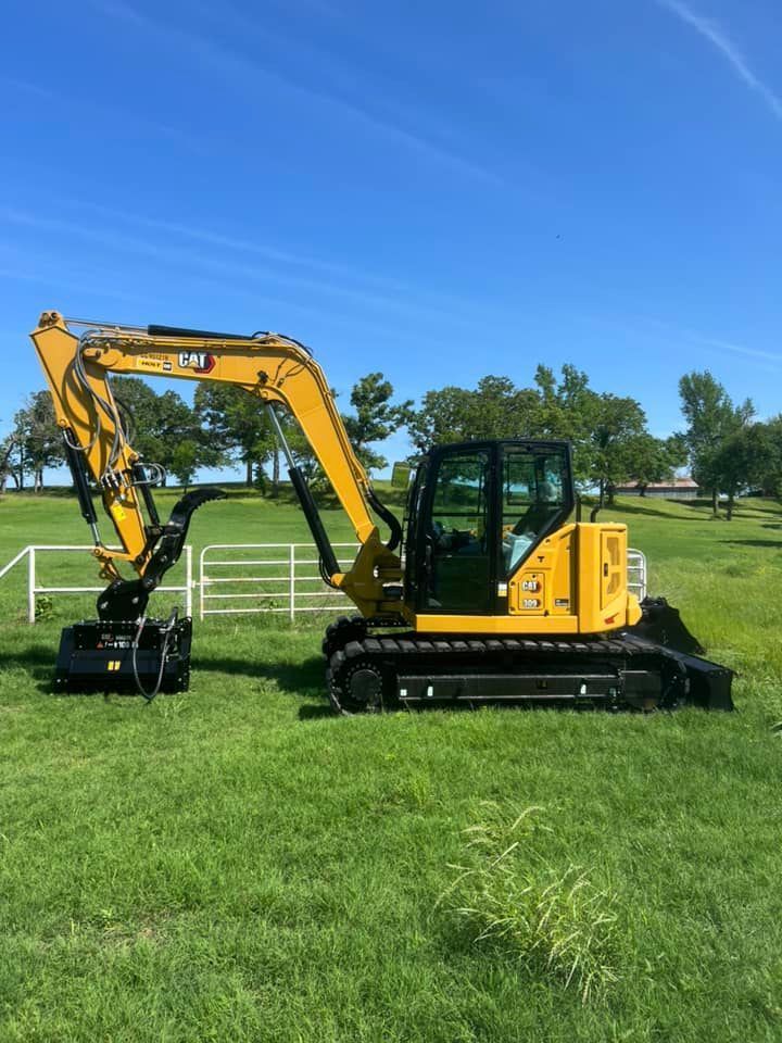 Yellow Caterpillar excavator on grass field under a blue sky.
