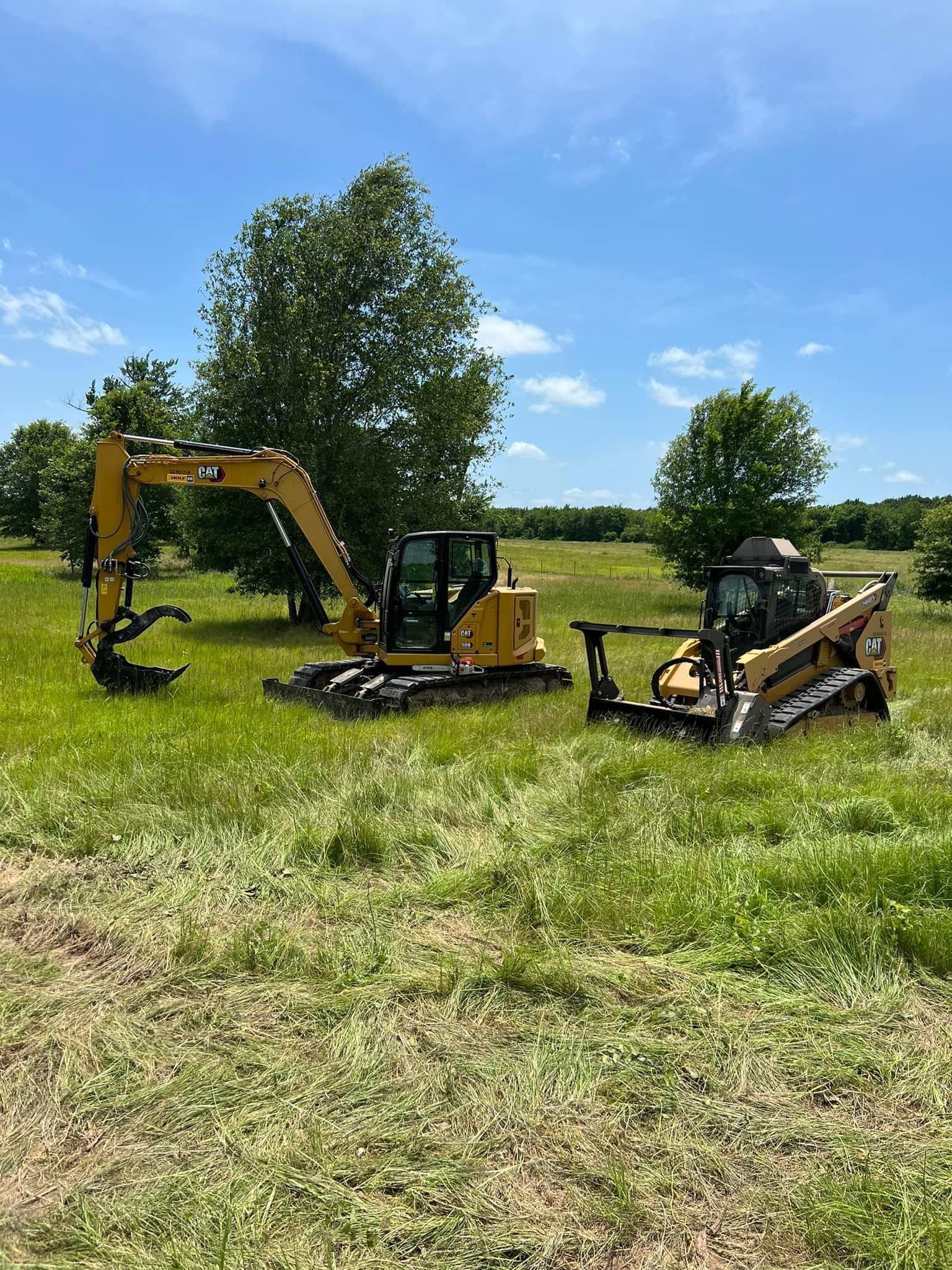 Yellow excavator and skid steer on a grassy field, with trees and blue sky in the background.